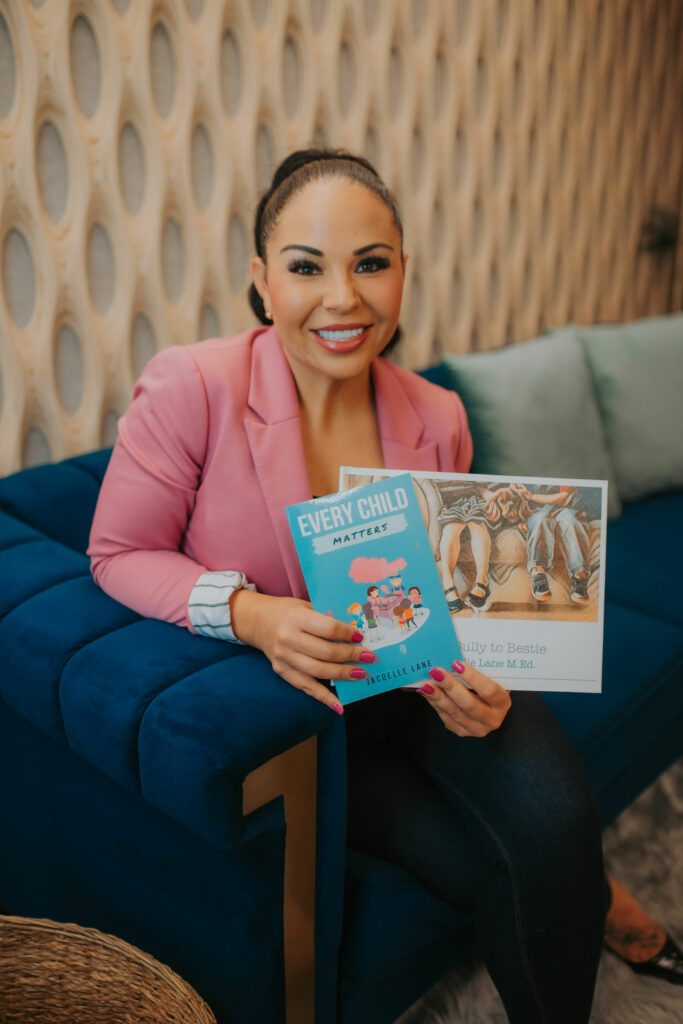 Jacqelle Lane on a couch displaying her books " Every Child Matters" and "From Bully To Bestie" - jacqelle lane